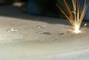 Close-up of a laser melting metal powder during a 3D printing process, creating sparks and partially fused powder on the surface.