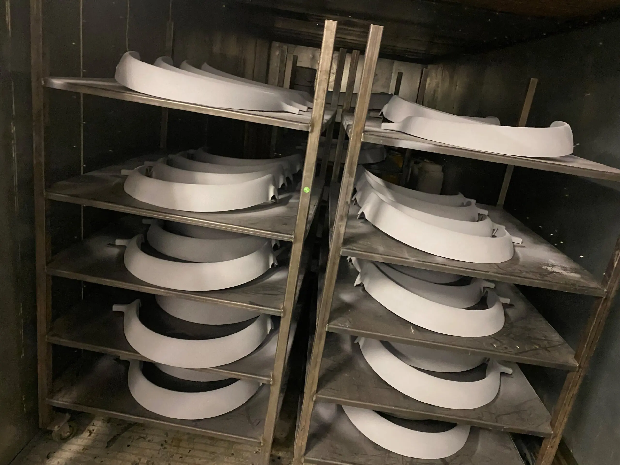 Stacks of white semi-circular curved components on metal shelves within an industrial oven or drying unit, likely mid-manufacturing.