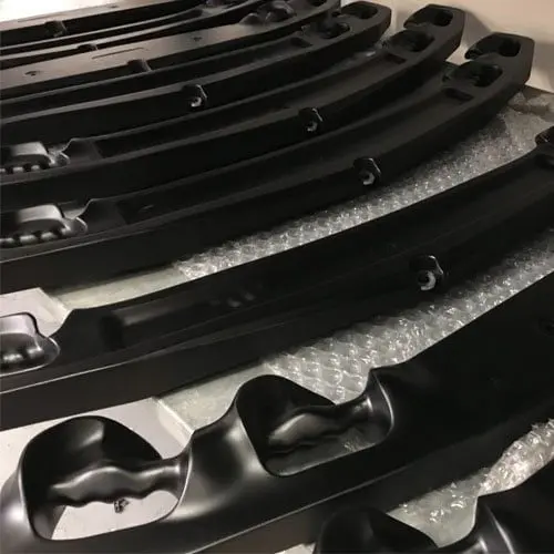 Rows of black curved plastic automotive parts placed on bubble wrap, showing smooth, contoured surfaces with grooves and attachment points.