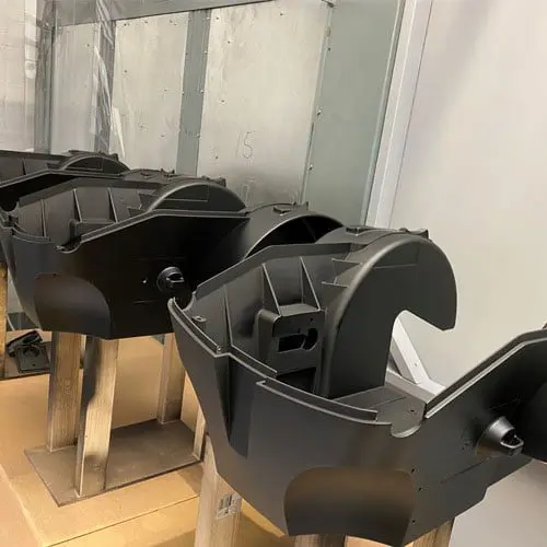 Black industrial plastic components mounted on wooden stands inside a manufacturing facility with metal walls.