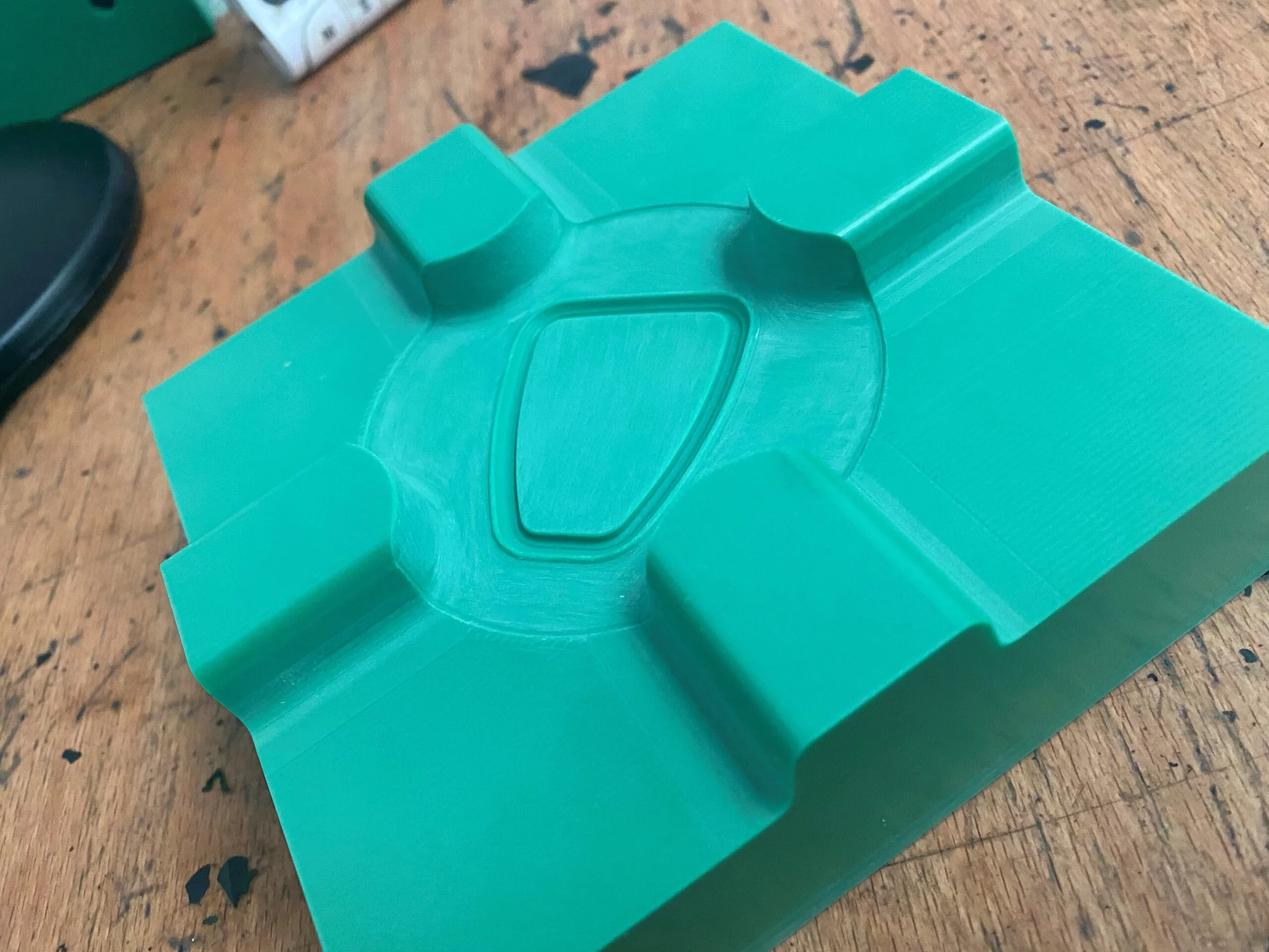 Green plastic mould featuring a central shield-shaped indent and four raised rectangular sections, placed on a wooden surface.