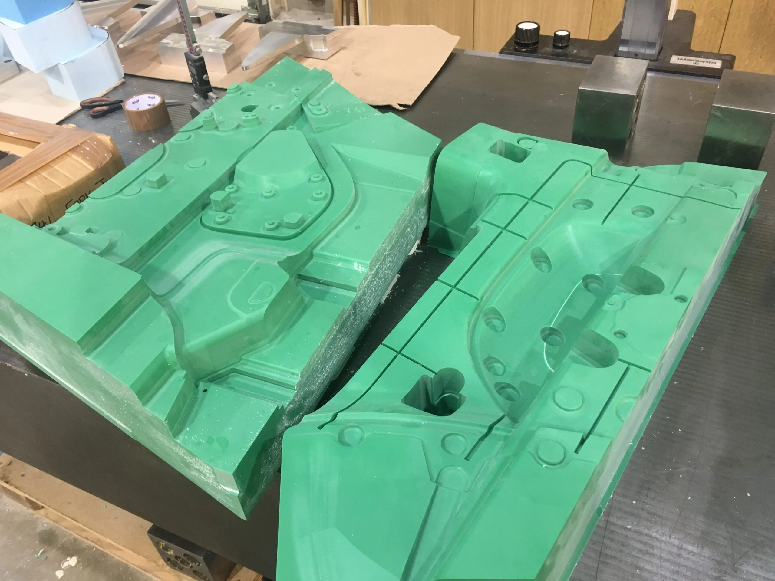 Two large green moulded foam parts with detailed recesses resting on a black worktable in a workshop setting.