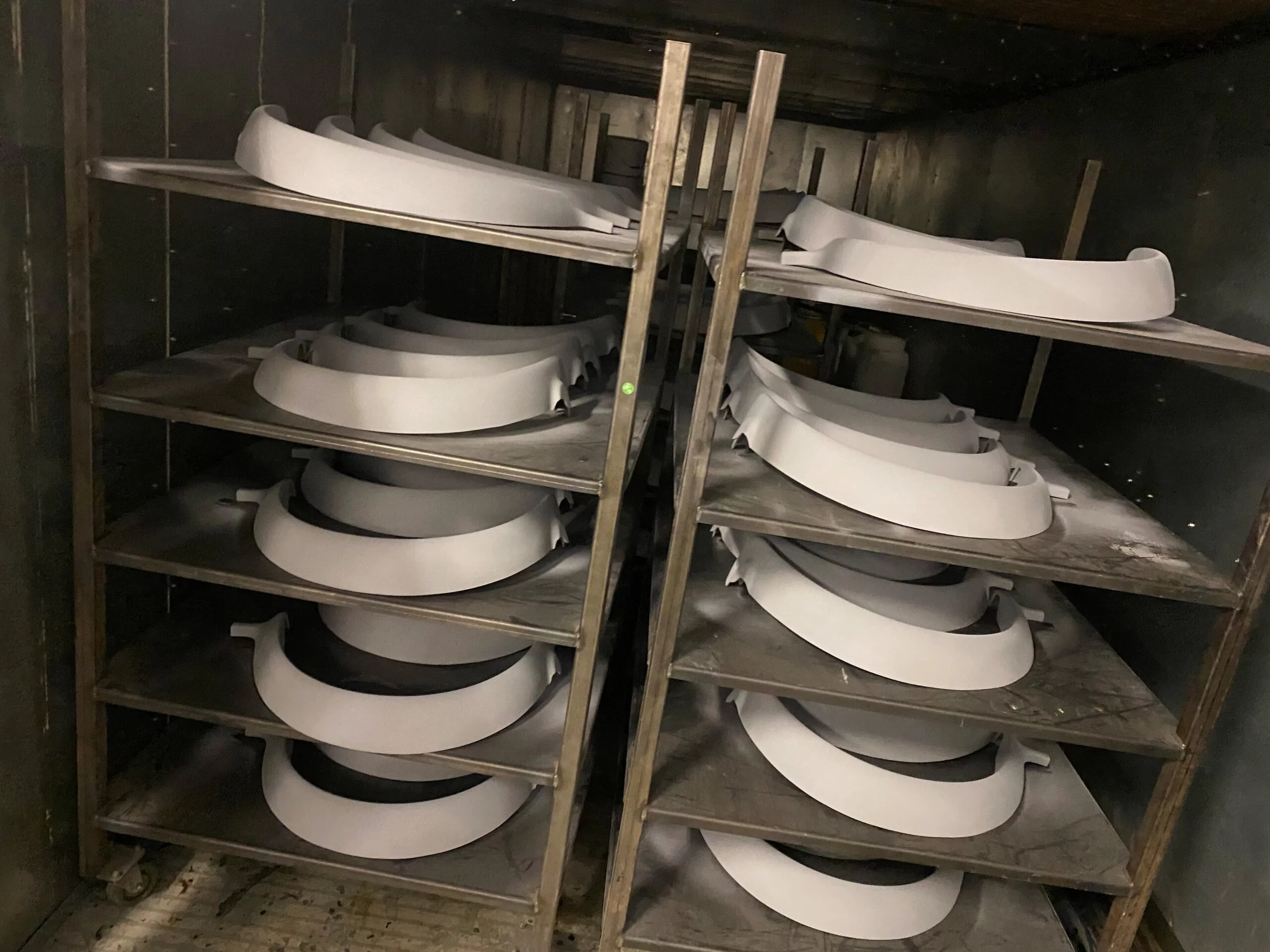 Stacks of white semi-circular curved components on metal shelves within an industrial oven or drying unit, likely mid-manufacturing.